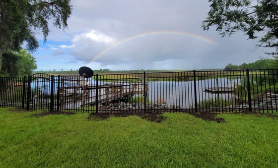 Black aluminum fence with an arched gate along a tidal creek, a rainbow over the marsh behind it