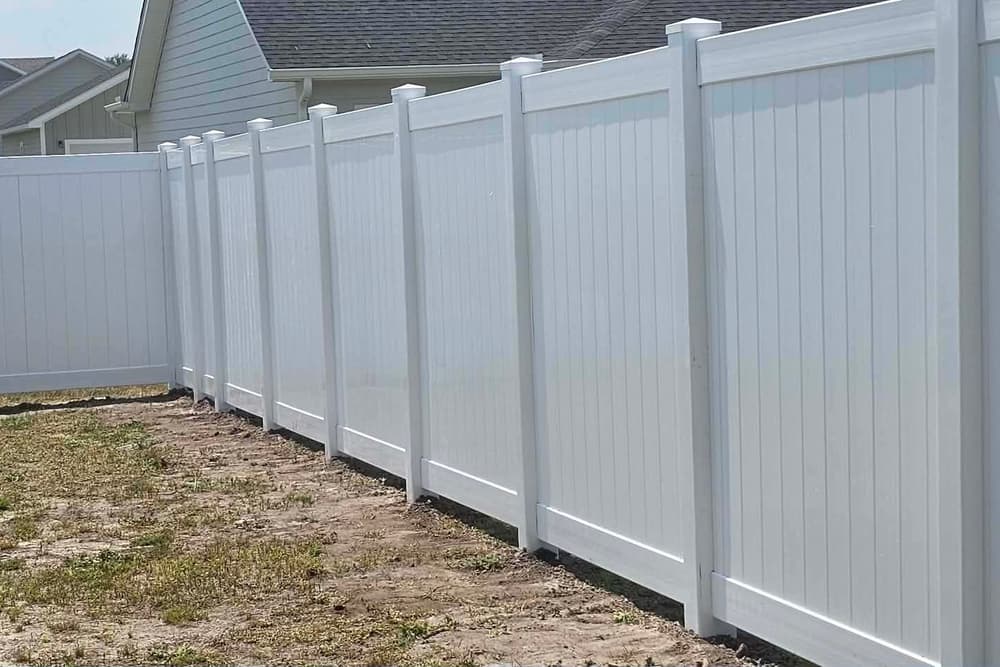 Long run of white vinyl privacy fence along the back of a lot in a newer subdivision