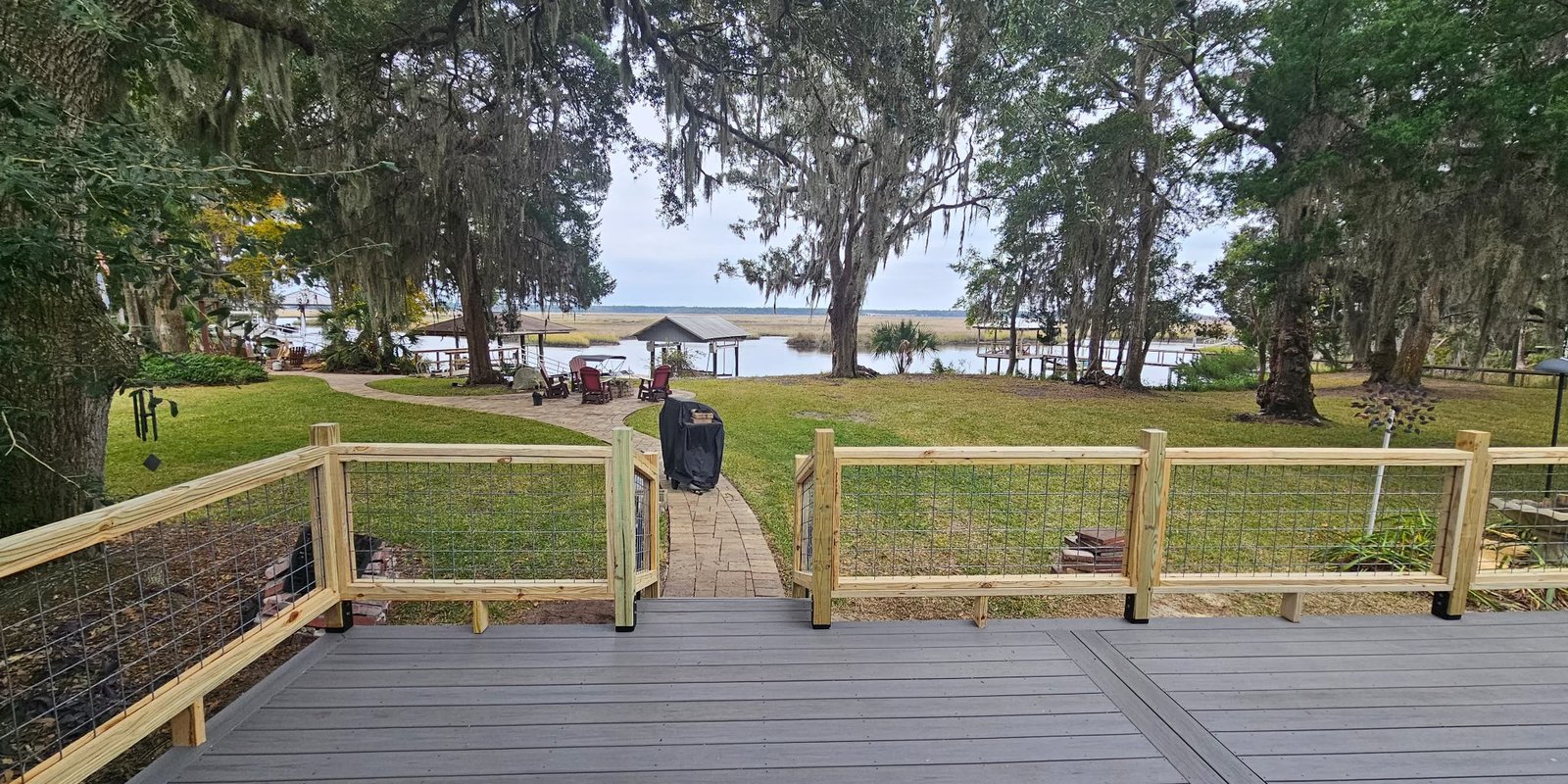 Gray composite deck with wood and wire railing overlooking a lawn, tidal river and mossy oaks