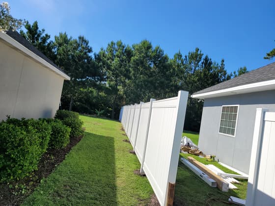 White vinyl privacy fence being installed between two houses, with bracing and offcuts still on the ground