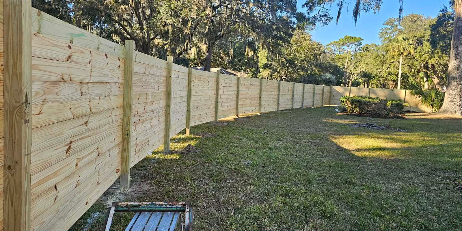 New wood privacy fence along a back yard shaded by live oaks hung with Spanish moss