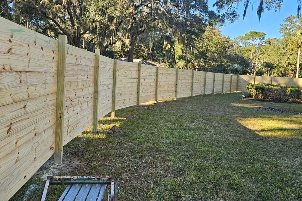 New wood privacy fence running the full width of a back yard under moss-hung oaks