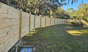 New wood privacy fence running the full width of a back yard under moss-hung oaks