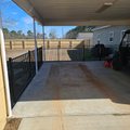 Black aluminum fence and gate enclosing a concrete carport slab with a wood privacy fence beyond