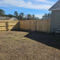 Corner of a new wood privacy fence with a gate in a bare winter yard beside a gray house