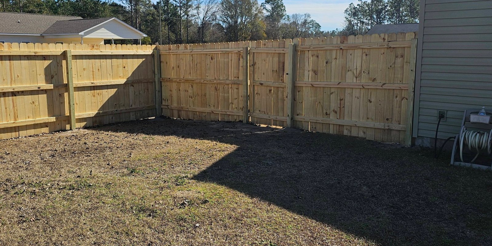 Corner of a new wood privacy fence with a gate in a bare winter yard beside a gray house