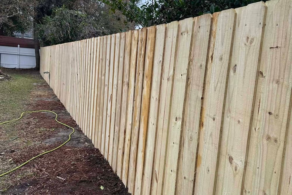 Tall board-on-board wood privacy fence in a long straight run with freshly dug soil at the base