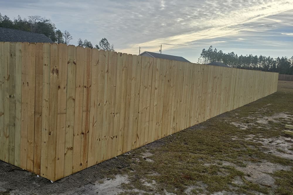 Long wood privacy fence at dusk on a new-build lot with sandy ground at its base