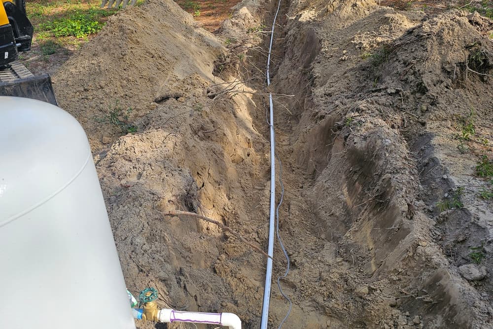 Open utility trench with pipe laid in the bottom and a mini excavator parked at the head of the run