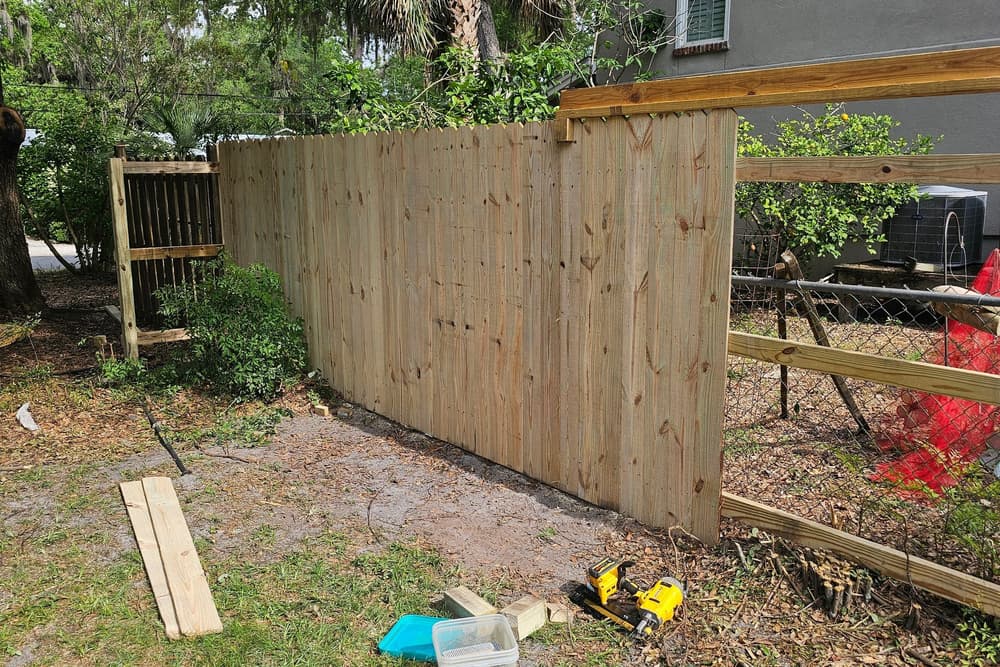 New pressure-treated wood privacy fence along a side yard with tools still on the ground