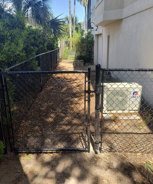 Black chain link fence and double gate closing a narrow side passage beside a house