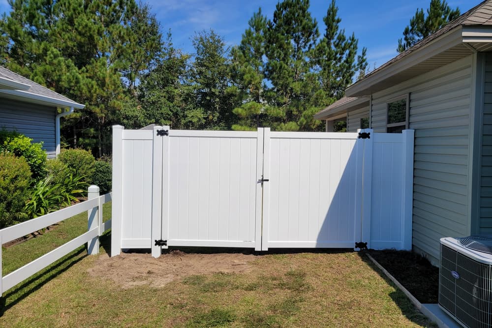 White vinyl privacy fence with a wide double gate between two houses