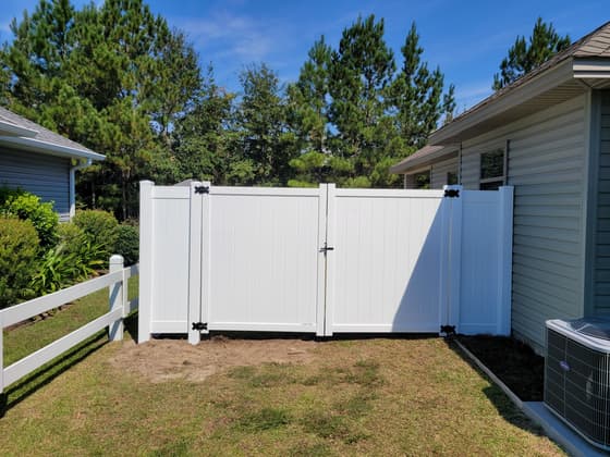 White vinyl privacy fence with a wide double gate between two houses
