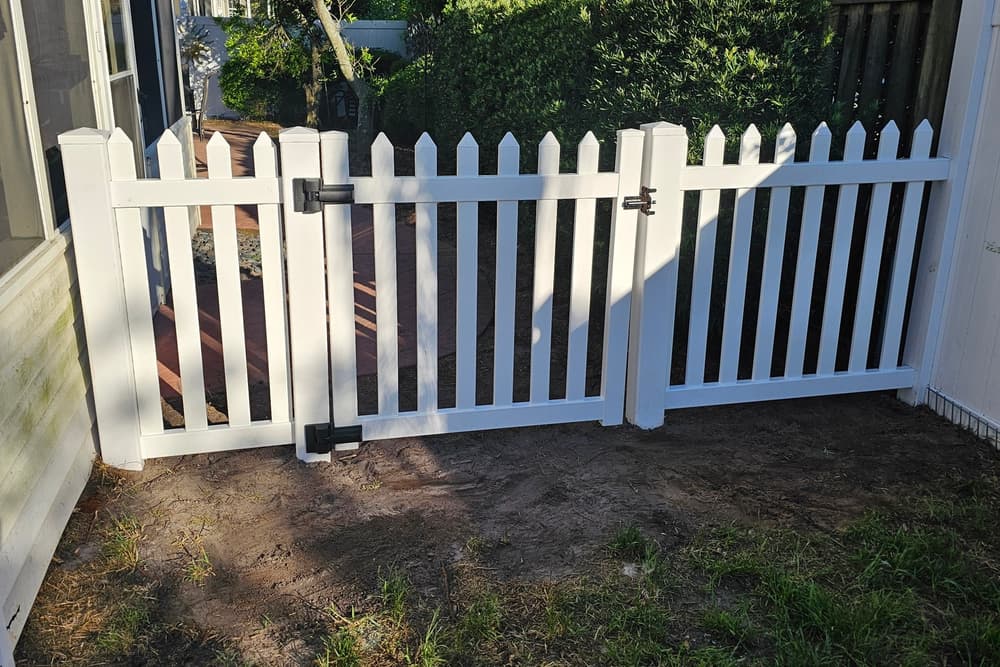 White vinyl picket fence with a scalloped top and a gate enclosing a small side yard